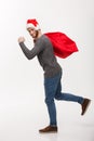 Christmas concept - Young confident beard man running and holding red big santa bag with a lot of present inside. Royalty Free Stock Photo