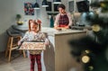 Christmas cookies preparation. Cute little girl with baking sheet full of homemade sweet ginger biscuits. She and mother preparing Royalty Free Stock Photo