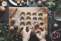 Christmas cookies. Top view of female hands holding, cooking raw unbaked biscuits in black plate with Christmas decoration