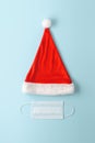 Christmas era covid concept. Medical protective mask and Santa Claus hat on pastel blue background. Royalty Free Stock Photo
