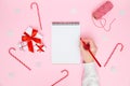 Christmas cozy background. Female hand writing in blank notebook with festive decorations, gift boxes on pastel pink Royalty Free Stock Photo