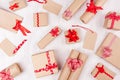 Christmas craft paper gifts with red ribbons and bows as festive pattern on soft white wooden background.