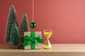 Christmas creative concept with gift box, pine trees and hourglass sand clock on wooden table over red background