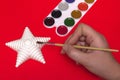 Christmas creativity on a red background woman paints a Christmas star, close-up top view