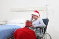 Christmas day isolated in hospital room with coronavirus, sad and pensive elderly woman on wheelchair with red hat and gift near Royalty Free Stock Photo