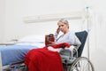 Christmas day isolated in hospital room with coronavirus, sad and pensive elderly woman on wheelchair with red hat and gift near Royalty Free Stock Photo