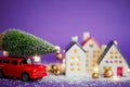 Christmas decor - red retro car on snow carries past houses with fairy lights in bokeh Christmas tree with gift boxes on roof. Toy Royalty Free Stock Photo