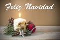 Christmas decoration with candle, pine, bauble, with text in Spanish `Feliz Navidad` in wooden background