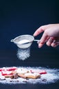 Christmas decoration and cookies.Woman hand sprinkling sugar on a cookies. Flour and spices for a baking on a dark backg Royalty Free Stock Photo