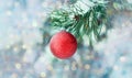 A Christmas decoration hanging on a snow-covered branch against a background of blurred festive lights. A red ball on the branch o Royalty Free Stock Photo