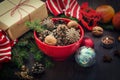 Christmas decoration - red bowl full of fir-cones, gift box wrapped in kraft paper, pine branches, candle, nuts, anise, apples, ch