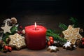 Christmas decoration with a red burning candle, gingerbread cookies, rose hips, branches and cones on a dark rustic wooden Royalty Free Stock Photo