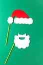 Christmas decoration, white beard and red Santas hat on sticks. Festive concept, party accessories. Vertical, flat lay. Minimal