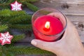 Christmas decorations, fir branches and cropped hand, holding red flaming candle on vintage wooden board background Royalty Free Stock Photo