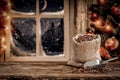 Christmas decorations and fresh coffee beans in jute sack with blurred christmas tree and night window background.