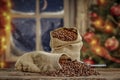 Christmas decorations and fresh coffee beans in jute sack with blurred christmas tree and sowy night window background.