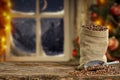 Christmas decorations and fresh coffee beans in jute sack with blurred christmas tree and sowy night window background.