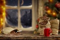 Christmas decorations and fresh coffee beans in jute sack with blurred christmas tree and sowy night window background.