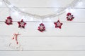 Christmas decorations with garland lights, red textile trees and stars, and wooden skates on white wooden boards background Royalty Free Stock Photo