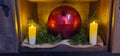 Christmas decorations with large red ball, candles, and greenery