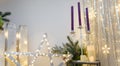 Christmas decorations. Purple candles in candlestick, fir tree branches and cones, siver curtains with shiny stars