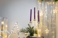 Christmas decorations. Purple candles in candlestick, fir tree branches and cones, siver curtains with shiny stars and garland