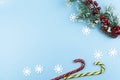 Christmas decorations, snowflakes, candy canes, fir tree branch and red berries on blue pastel background. Christmas holiday