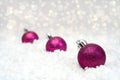 Christmas decorations on a white background. Three crimson shiny balls lie on the white snow. Bokeh in the background.