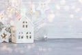 Christmas decorative house, glass balls and garland lights on white wooden background