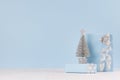 Christmas decorative silver tree with gifts and ribbons on white wood table and pastel blue wall.