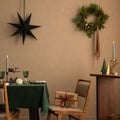 Christmas dining room interior with table, green tablecloth, wooden console, christmas wreath, chair, gifts, candle with Royalty Free Stock Photo