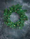 Christmas door wreath made of green tree fir branches and light garlands on dark grey wooden background Royalty Free Stock Photo