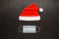 Christmas era covid concept. Medical protective mask and Santa Claus hat on a dark brown background.