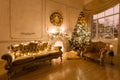 Christmas evening by candlelight. classic apartments with a white fireplace, decorated tree, sofa, large windows and Royalty Free Stock Photo