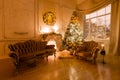 Christmas evening by candlelight. classic apartments with a white fireplace, decorated tree, sofa, large windows and Royalty Free Stock Photo