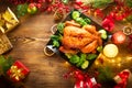 Christmas family dinner. Roasted chicken on holiday table, decorated with gift boxes, burning candles and garlands Royalty Free Stock Photo