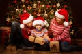 Christmas Family Open Present Gift front of Xmas Tree, Happy Parents with Child in Santa Hats Royalty Free Stock Photo