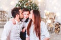 Christmas family smiling and kissing near the Xmas tree. Living room decorated by Christmas tree and present gift box