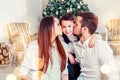 Christmas family smiling and kissing near the Xmas tree. Living room decorated by Christmas tree and present gift box