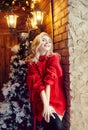 Christmas Fashion woman blonde in the red sweater, having fun and posing against the Christmas tree and lamppost. Winter