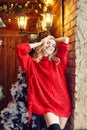 Christmas Fashion woman blonde in the red sweater, having fun and posing against the Christmas tree and lamppost. Winter