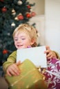 Christmas, festive and a boy opening a present under a tree in the morning for celebration or tradition. Kids, gift and Royalty Free Stock Photo