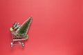 Christmas fir and silver bow for gift in toy shopping cart on burgundy background, copy space. Festive, New Year, sales, online