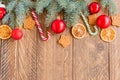 Christmas fir-tree branches with baubles, candy canes, dry oranges and star shape cookies on wooden background with copy space Royalty Free Stock Photo