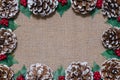 Christmas flat-lay frame of pinecones, holly leaves, and red berries on rustic fabric background Royalty Free Stock Photo