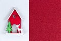 Christmas flatlay layout. wooden toy house, a deer and a Christmas tree on a red glitter shiny background. Christmas card with Royalty Free Stock Photo