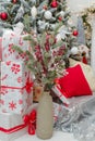 Christmas floral composition, bouquet of branches with red berries in vase with wrapped present boxes, cushions and decorated fir Royalty Free Stock Photo