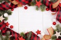 Christmas frame of ornaments, branches, burlap and red and black buffalo plaid ribbon, overhead view on a white wood background