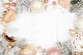 Christmas frame of snowy branches and dusty rose, gold, and white ornaments on a white wood background