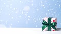 Christmas gift box with green ribbon bow in snow on blue background. Christmas, New Year, winter holidays concept Royalty Free Stock Photo